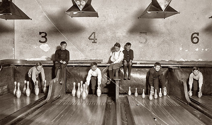 A black and white photos of boys setting up bowling pins at an old bowling alley